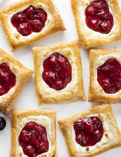 small pastries with cherries on them sitting on a white plate next to some grapes