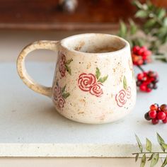 a coffee cup sitting on top of a counter next to some red berries and greenery