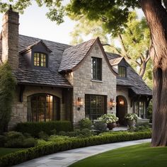 a stone house with two large windows and lots of greenery on the front lawn