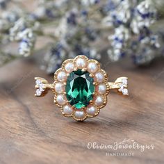 a green ring with pearls on it sitting next to some blue and white flower buds