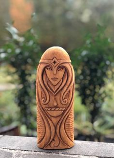 a carved wooden object sitting on top of a stone wall with trees in the background