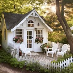 a small white house with flowers in the window and chairs on the front porch next to it