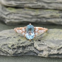 an oval blue topazte ring with diamond accents sits on a rock in front of some rocks