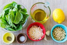 ingredients to make spinach salad laid out in bowls on a wooden surface with lemons, olive oil, and basil leaves