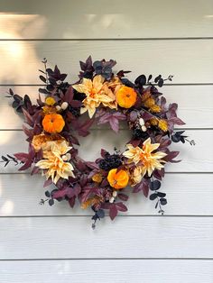 a wreath with orange and yellow flowers hanging on the side of a white house wall