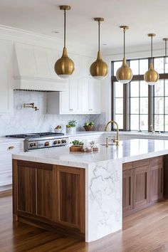 a kitchen with marble counter tops and gold pendant lights hanging from the ceiling over the island