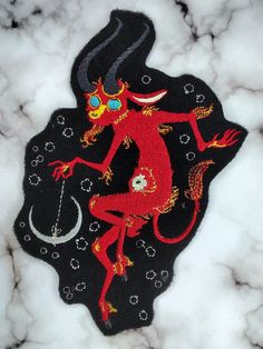 an embroidered patch with a red devil on it's back and the moon in the background