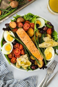 a salad with salmon, eggs, tomatoes and other vegetables on a white plate next to a glass of orange juice