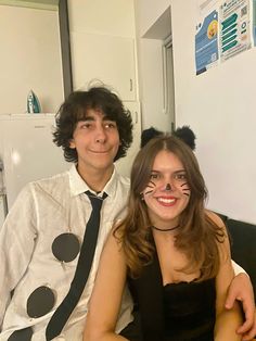 a man and woman dressed up as cats sitting next to each other in front of a refrigerator