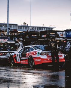 two men standing next to each other in front of race cars on a wet track