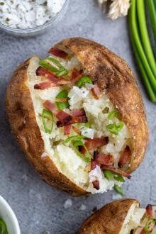 two baked potato halves with bacon and green onions on the side next to dips