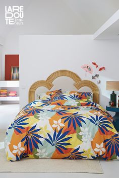 a bed with colorful sheets and pillows in a room that has white walls, flooring and furniture