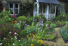 a garden filled with lots of flowers next to a stone building and white trimming