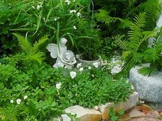 a garden filled with lots of green plants and white flowers next to a stone statue