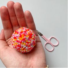 a hand holding a small ball of sprinkles next to a pair of scissors