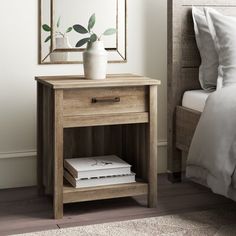 a nightstand with two books and a vase on it next to a bed in a bedroom