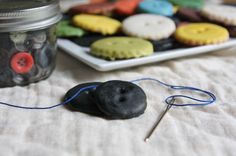 there are some cookies and buttons on the table next to a glass jar with pins