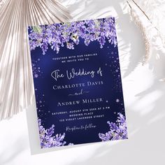 a wedding card with purple flowers on the front and blue back, sitting next to some palm fronds