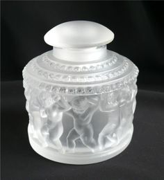 a white glass jar with an angel design on the front and bottom, sitting on a black surface