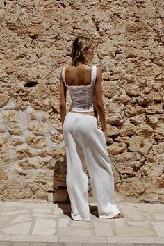 a woman standing in front of a stone wall with her back turned to the camera