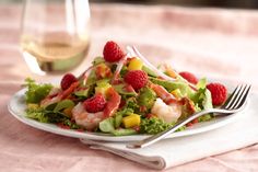 a salad with shrimp, raspberries and avocado on a plate next to a glass of wine