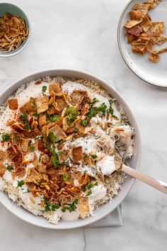 a bowl filled with rice and toppings on top of a white table next to bowls of chips