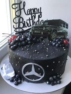 a birthday cake decorated with black frosting and blueberries is displayed in front of a window