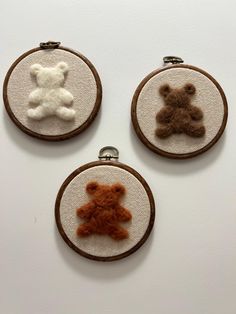 three embroidered teddy bears are hanging on small hoop frames, one is brown and the other is white