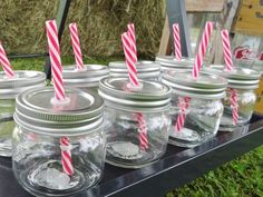 mason jars filled with candy canes on top of a black table in front of hay bales