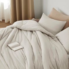 an unmade bed with beige sheets and pillows on the floor next to a window