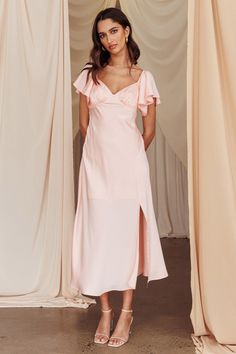 a woman standing in front of curtains wearing a pink dress with ruffles on the shoulders