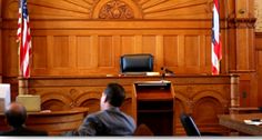 two men sitting at desks in front of an american flag and wooden paneled wall