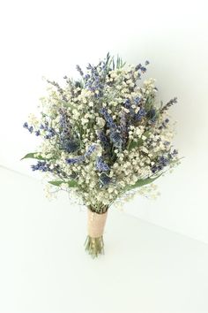 a bouquet of blue and white flowers in a vase on a table with a white wall behind it