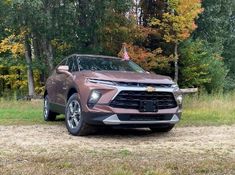 the front end of a silver chevrolet suv parked in a field with trees and grass