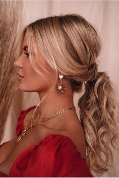 a woman with blonde hair wearing gold earrings and a red dress looking off to the side