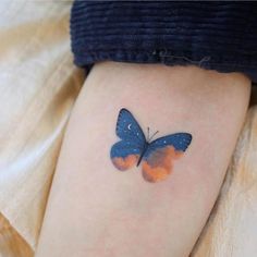 a blue and orange butterfly tattoo on the right thigh, with black dots around it