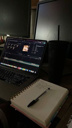 an open laptop computer sitting on top of a desk next to a notebook and monitor