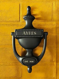 a black door handle on a yellow brick wall with the name ayrs written on it