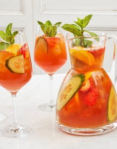 two glasses filled with water and fruit next to each other on a marble counter top