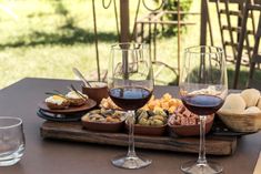 two glasses of wine sitting on top of a wooden tray filled with food and snacks