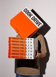 a man holding stacks of orange and white books in front of his face with the words cook drive written on them