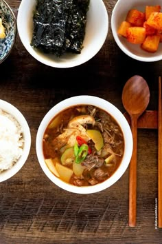 bowls of food and chopsticks sit on a wooden table next to rice, broccoli, and other foods