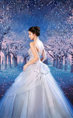 a woman in a white dress standing in front of trees with pink and blue flowers