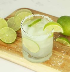 a margarita with limes and salt on a cutting board next to some tortilla chips