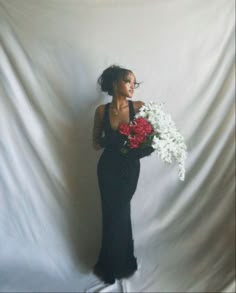 a woman in a black dress holding flowers and posing for the camera on a white background