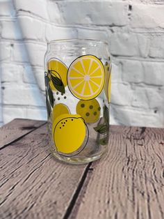 a glass with lemons and leaves painted on it sitting on top of a wooden table