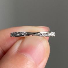 a close up of a person's hand holding a wedding band that has three diamonds on it