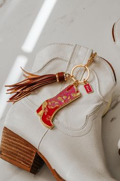 Sparkly and country chic, our Texas-sized statement keychain in Rodeo Glam Boot features a floral motif and sparkles aplenty, a design inspired by rodeo cowgirls and shimmering diamonds. Our Rodeo & Roses keychain includes one cowgirl boot, one SCL logo charm, a lobster claw clasp and tassel. The cowgirl boot charm is 3" tall and 1.75" wide. Our fashion keychain's color palette features bright pink hues with gold and cranberry accents and a caramel brown tassel.  Presented in our signature pouch within an SCL logo box--an exquisite choice for effortless and refined gifting. Custom designed and assembled in the USA 2D soft enamel charms with gold tone plating Boot charm is 3" tall, keychain ring and clasp add 3.5 inches when hung Glam Cowgirl, Rodeo Gifts, Rodeo Cowgirl, Cowgirl Boot, Charm Keychain, Caramel Brown, Cow Girl, Soft Enamel, Enamel Charms