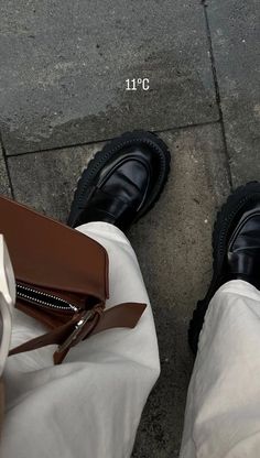 a person wearing white pants and black shoes standing next to a brown bag on the sidewalk