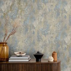 a table topped with books and vases next to a wallpaper covered in dirt